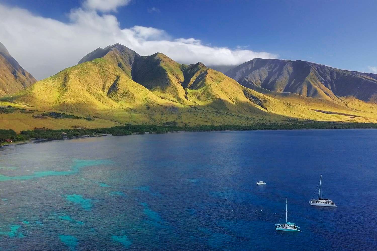 West Maui mountains above a turquoise reef and catamarans on the blue ocean
